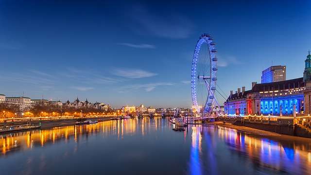London Eye bei Nacht, beleuchtet, reflektiert im Wasser, umgeben von der Themse und städtischer Architektur, in der Nähe von Stratlane-Zertifizierungsbüro.