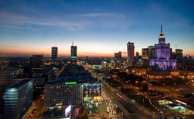 Skyline von Warschau bei Sonnenuntergang mit modernen Gebäuden, darunter das Kultur- und Wissenschaftszentrum, Werbung auf einem Hotel und sanften Lichtveränderungen am Himmel.