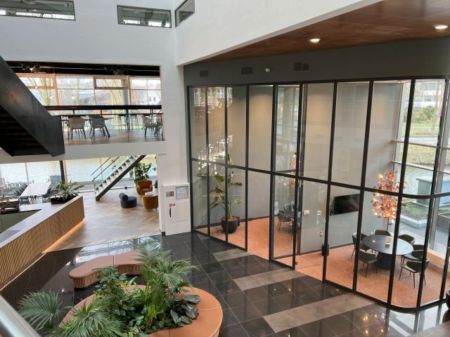 Moderne Büroeinrichtung im Stratlane Hauptsitz in Amsterdam mit Blick auf den Innenbereich, Pflanzen, Sitzbereichen und einem gläsernen Konferenzraum.