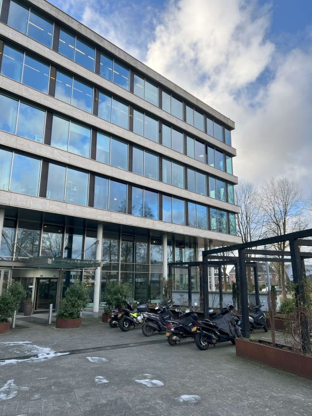 Moderne Bürogebäude in Amsterdam mit großen Fensterfronten, Eingangsbereich und geparkten Motorrädern im Vordergrund.