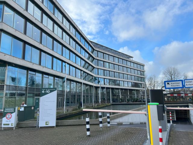 Bürogebäude in Amsterdam mit Glasfassade, Standort von Stratlane Certification BV, nahe Flughafen, inklusive Parkplatz und Zugangsschranke.