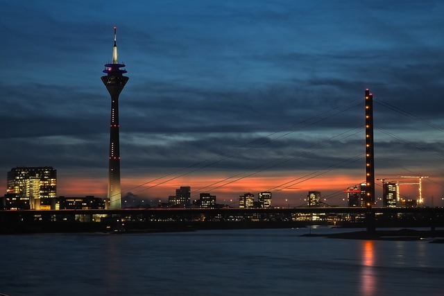 Düsseldorf skyline at dusk featuring the Rheinturm and illuminated bridge over the Rhine River, symbolizing the city’s modern infrastructure and vibrant atmosphere.