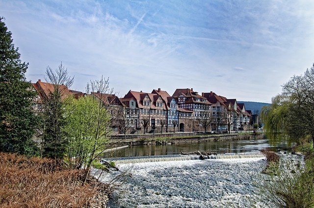 Historische Fachwerkhäuser entlang des Wassers in Fulda, umgeben von Bäumen und einem kleinen Wasserfall, symbolisieren die regionale Identität und den Standort von Stratlane Certification.