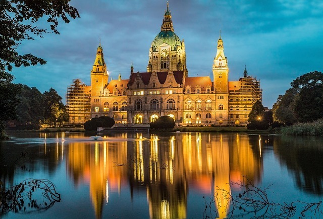 Hannover Neues Rathaus bei Nacht, beleuchtet und reflektiert im Wasser, umgeben von Bäumen, symbolisiert die zentrale Rolle von Stratlane Certification in Hannover.