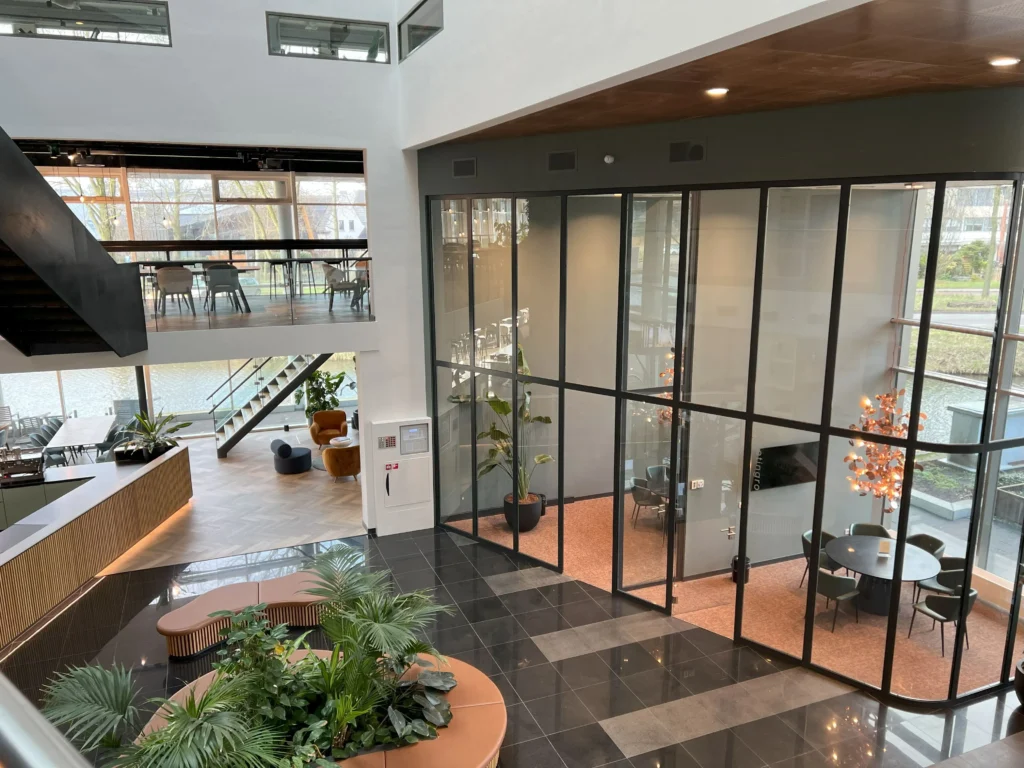 Modern interior with glass walls, greenery, seating areas, and a staircase.